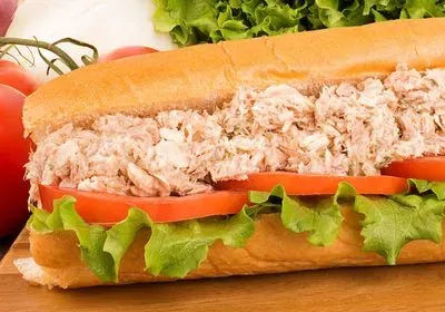 a tuna salad sub with lettuce and tomato on a wooden board with fresh veggies in the background